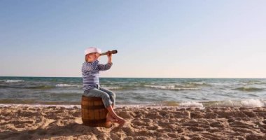 Happy child pretend to be sailor. Kid having fun at beach. Boy looking through spyglass. Summer vacation and travel concept. Slow motion