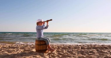 Happy child pretend to be sailor. Kid having fun at beach. Boy looking through spyglass. Summer vacation and travel concept. Slow motion