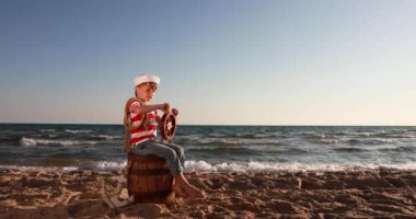 Happy child pretend to be sailor. Kid having fun at beach. Boy holding wheel of ship. Summer vacation and travel concept. Slow motion