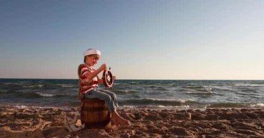 Happy child pretend to be sailor. Kid having fun at beach. Boy holding wheel of ship. Summer vacation and travel concept. Slow motion