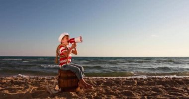 Happy child pretend to be sailor. Kid having fun at beach. Boy shouting through loudspeaker. Summer vacation and travel concept. Slow motion