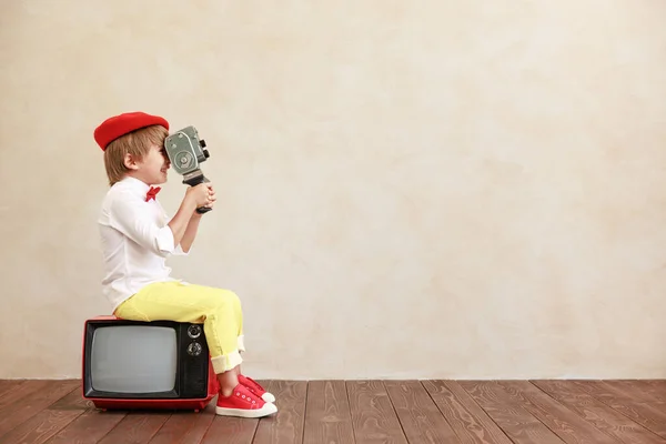 有趣的男孩拿着老式相机面对着发牢骚的墙壁背景 坐在老电视上的孩子在家里玩耍的孩子 — 图库照片