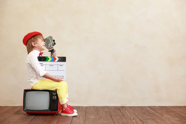 有趣的男孩拿着老式相机和拍手在格子墙的背景上 坐在老电视上的孩子在家里玩耍的孩子 — 图库照片