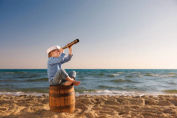 小孩假装是水手 小孩透过望远镜看 小孩坐在海滩上的旧木桶上 男孩在暑假 冒险和旅行概念 — 图库照片