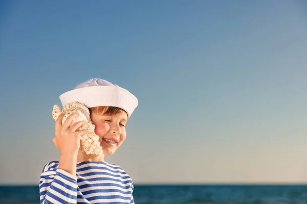 快乐的孩子在海滩上听着贝壳 男孩在蓝色的大海和天空背景下的肖像 孩子们暑假过得很开心 梦想和想象的概念 — 图库照片