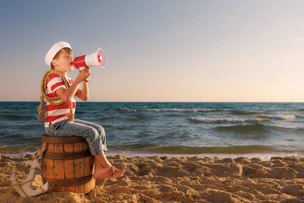 子供は船員のふりをする 子供がスピーカーを持ってる 子供はビーチの古い樽の上に座っている 夏休みに男の子 冒険と旅行のコンセプト — ストック写真