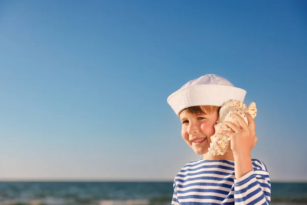 幸せな子供はビーチで貝殻を聞く 青い海と空の背景に対する少年の肖像画 夏休みを楽しんでいる子供 夢と想像力の概念 — ストック写真