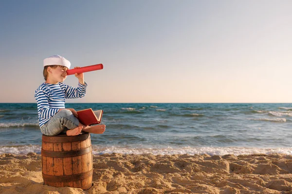 子供は船員のふりをする スパイガラスを通して見ている子供 子供はビーチの古い樽の上に座っている 夏休みに男の子 冒険と旅行のコンセプト — ストック写真