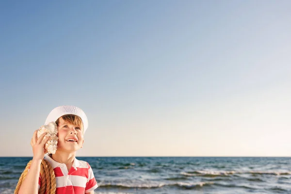快乐的孩子在海滩上听着贝壳 男孩在蓝色的大海和天空背景下的肖像 孩子们暑假过得很开心 梦想和想象的概念 — 图库照片