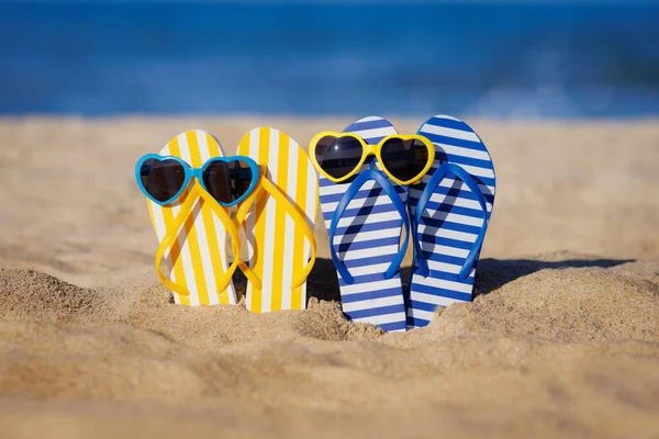 青い海の背景に対して黄色の砂の上にフリップフロップとサングラス 夏休みと旅行のコンセプト — ストック写真
