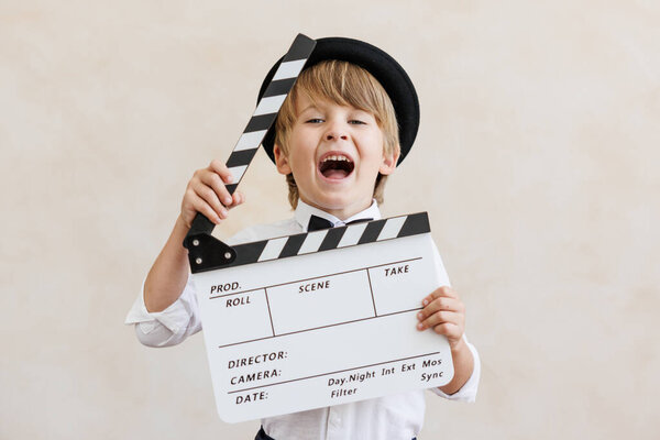 Director shouting against grunge wall background. Boy playing in home. Child wearing vintage costume. Kid holding clapper. Social media and Internet nerwork concept