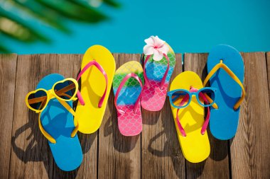 Plaj terlikleri ve tahta arka planda güneş gözlüğü. Yüzme havuzunun mavi suyuna karşı tatil malzemeleri. Yaz tatili ve seyahat konsepti