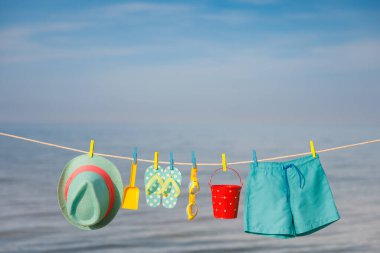 Plaj şapkası, parmak arası terlikler ve çamaşır ipinde asılı gözlükler. Mavi gökyüzüne ve denize karşı tatil şeyleri. Yaz tatili ve seyahat konsepti