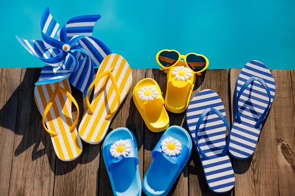 在木制背景上的海滩拖鞋和太阳镜 在游泳池蓝色水边度假用的东西 暑假和旅行概念 图库图片