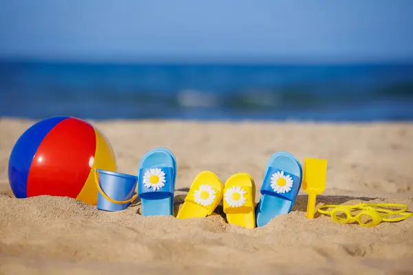 青い海の背景に対して黄色の砂の上の子供たちのフリップフロップ ビーチボール シュノーケリング 夏休みのコンセプト ロイヤリティフリーのストック写真
