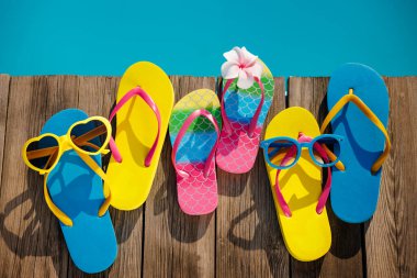 Plaj terlikleri ve tahta arka planda güneş gözlüğü. Yüzme havuzunun mavi suyuna karşı tatil malzemeleri. Yaz tatili ve seyahat konsepti