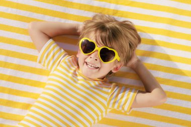 Mutlu çocuk plaj havlusunda yatıyor. Yaz tatilindeki komik çocuk. Çocuk yaz tatilinde eğleniyor. Üst görünüm portresi