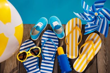 Plaj terlikleri ve tahta arka planda güneş gözlüğü. Yüzme havuzunun mavi suyuna karşı tatil malzemeleri. Yaz tatili ve seyahat konsepti