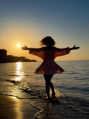 Kumsalda dans eden genç bir kadının silueti. Yaz tatilleri konsepti