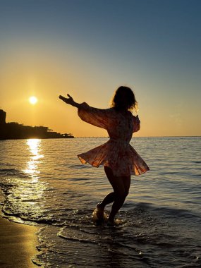 Kumsalda dans eden genç bir kadının silueti. Yaz tatilleri konsepti