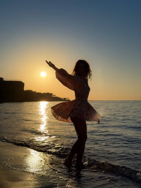 Kumsalda dans eden genç bir kadının silueti. Yaz tatilleri konsepti