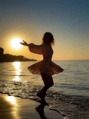 Kumsalda dans eden genç bir kadının silueti. Yaz tatilleri konsepti
