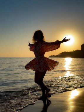 Kumsalda dans eden genç bir kadının silueti. Yaz tatilleri konsepti