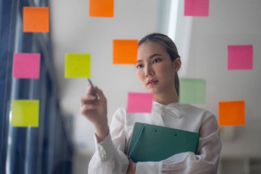 Bir iş kadını fikir alışverişinde bulunmak için post-it kullanır, beyin fırtınası kavramını gözler önüne serer. Yapışkan notlar cam bir duvara yerleştirilmiş.