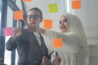 İş adamları toplantı odasında buluşup yaratıcı bir beyin fırtınası sürecinin bir parçası olarak fikirleri paylaşmak ve rafine etmek için yapışkan notlar kullanıyorlar.