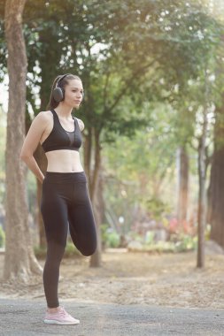 Koşu için giyinmiş genç bir bayan atlet parkta koşuya hazırlanırken bacaklarını esnetirken görülüyor.