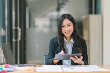 Modern ofisteki masada dijital tablet kullanan Asyalı güzel bir iş kadını.