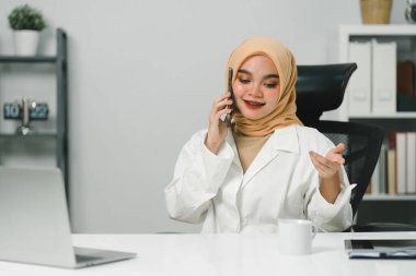 Çekici, genç Müslüman bir iş kadını modern bir ofiste akıllı telefonuyla konuşuyor.
