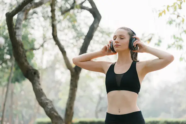 stock image A relaxed woman is shown enjoying music while jogging through a public park. The young lady is feeling free, relaxed, and happy