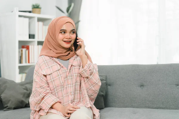 Hermosa Chica Musulmana Usando Hijab Hablando Teléfono Inteligente Casa Sentada —  Fotos de Stock