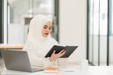 Ofiste, tesettürlü Müslüman bir işkadını bilgisayarının başında özenle çalışıyor, profesyonelliğini ve işine bağlılığını gösteriyor