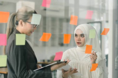 İş adamları toplantı odasında buluşup yaratıcı bir beyin fırtınası sürecinin bir parçası olarak fikirleri paylaşmak ve rafine etmek için yapışkan notlar kullanıyorlar.