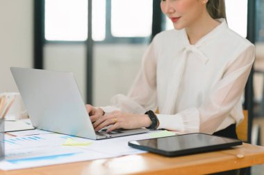 Asyalı güzel bir iş kadınının modern bir ofisteki masasında dijital bir dizüstü bilgisayar kullanırken görüntüsü.