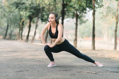 Spor giyim sektöründe güzel bir sporcu kadın yüzünde bir gülümsemeyle vücudunu esnetirken, Autumn City Park arka planında antrenman yapmadan önce ısınmak için esneklik egzersizleri yapıyor.