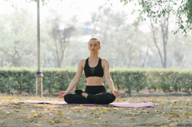 Spor giyim sektöründe güzel bir sporcu Autumn City Park arka planında nefes egzersizi yapıyor.