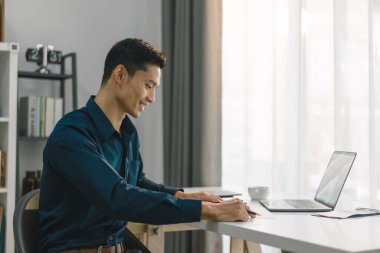 Genç bir iş adamının ev ofisindeki bir dizüstü bilgisayarda çalıştığı görülüyor. Görüntü, evden çalışma kavramını temsil ediyor.