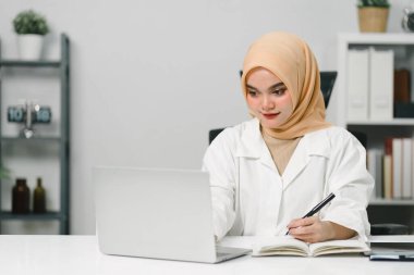 Başörtüsü takan güzel Müslüman iş kadını bilgisayarının başında özenle çalışıyor. İşine bağlılığını ve profesyonelliğini gösteriyor.