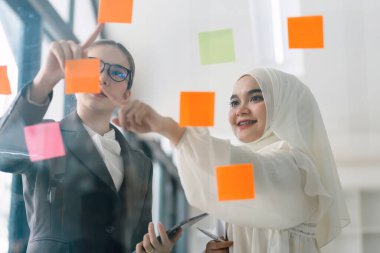 İş adamları toplantı odasında buluşup yaratıcı bir beyin fırtınası sürecinin bir parçası olarak fikirleri paylaşmak ve rafine etmek için yapışkan notlar kullanıyorlar.