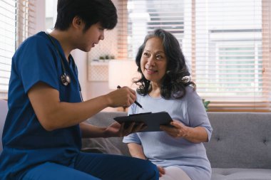 Bir sağlık ziyaretçisi, evdeki kanepede steteskop kullanan hasta yaşlı bir kadını muayene ediyor. Bu sahne evde sağlık hizmetleri kavramını gösteriyor.