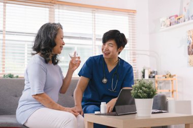 Bir sağlık ziyaretçisi elinde tabletle, yaşlı bir kadına ilaçlarını nasıl alacağını açıklarken görülüyor.