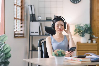 Mutlu ve rahat Asyalı iş kadınının portresi akıllı telefonuyla ev ofisinden uzaktan çalışıyor.