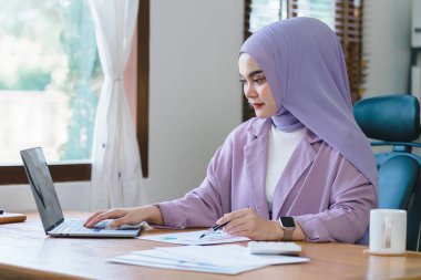 Memleketinden uzaktan çalışan, güzel bir Müslüman milenyum Asyalı iş kadını mor tesettürlü bir portrede resmediliyor.