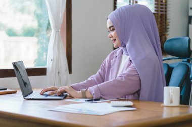 Bin yıllık Müslüman bir iş kadınının ev ofisinden uzaktan çalışan mor bir tesettüre bürünmüş görüntüsü.