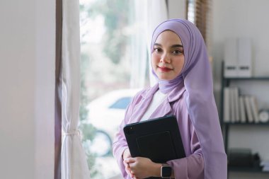 Mor tesettüre sahip Asyalı güzel bir iş kadınının portresi ev ofisinden uzaktan çalışıyor.