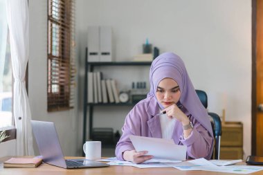 Mor tesettürlü Müslüman kadın evinden bilgisayarına bakarken stresli ve bitkin görünüyor.