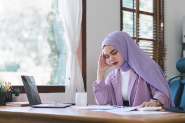 Stresli Müslüman milenyum iş kadını evde çalışan mor bir başörtüsü takıyor endişeli, yorgun ve bunalmış görünüyor.